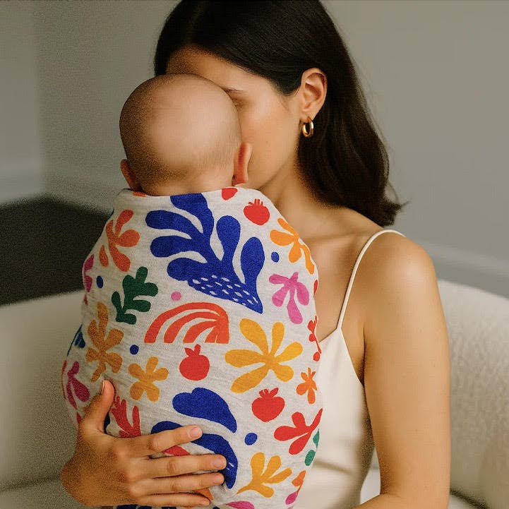 Mother holding baby wrapped in colourful organic muslin swaddle